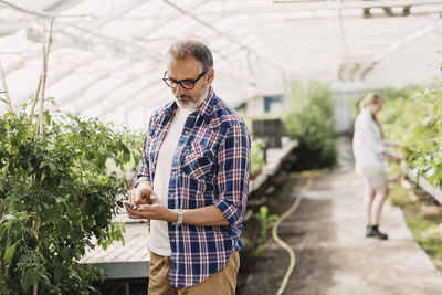Mature man using smart phone while standing in greenhouse