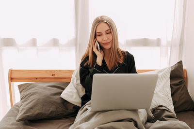 Young woman using phone while sitting on bed at home