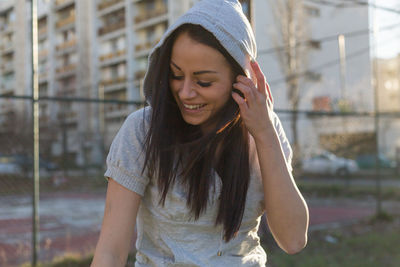 Close-up of smiling young woman wearing hood clothing against building