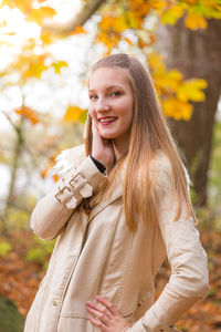 Portrait of young beautiful woman with straight blond hair standing against tree during autumn