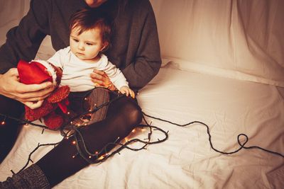 High angle view of baby with mother on bed holding illuminated light at home