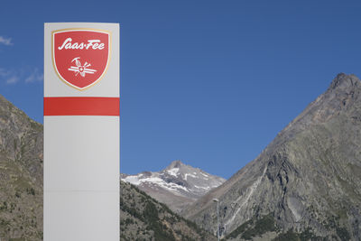 Road sign by mountains against clear blue sky