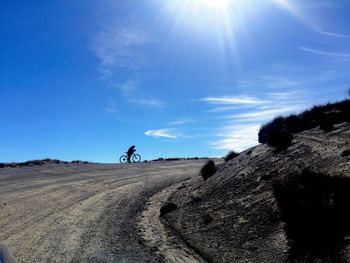 Man riding bicycle on dirt road against blue sky