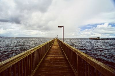 Pier on sea against cloudy sky