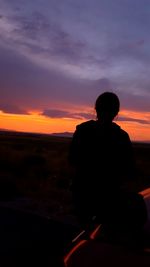 Silhouette of man sitting against orange sunset sky