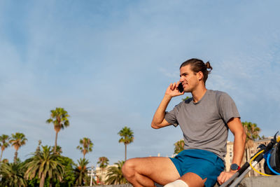 Young man using mobile phone while sitting against sky