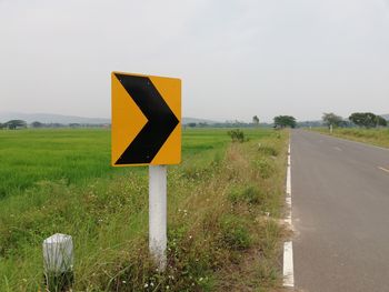 Road sign on field against sky