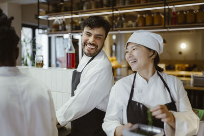 Smiling mature chef enjoying with male colleague at commercial kitchen in restaurant