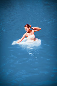 Bride wearing wedding dress while swimming in pool
