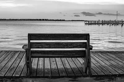 Empty bench on pier by sea against sky