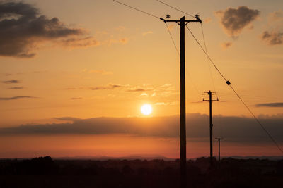 Silhouette electricity pylon against romantic sky at sunset