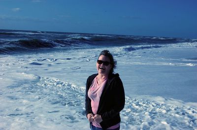 Portrait of woman in sunglass standing at beach against sky