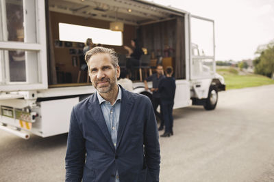 Portrait of confident businessman standing on road with colleagues and portable office truck in background