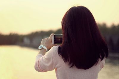 Rear view of woman photographing against sky during sunset