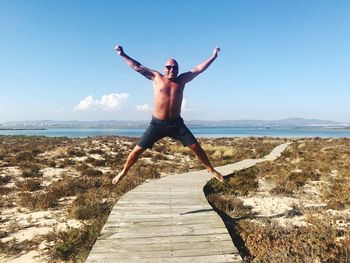 Full length of shirtless man at sea shore against sky