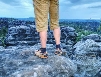 Low section of man standing on rock by sea against sky