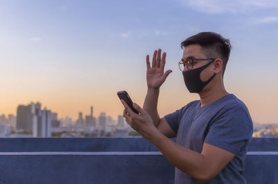 Asian man wearing face mask to protect from virus and make a video call with smartphone.