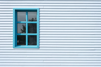 Side of a clapboard building with a window, painted blue.