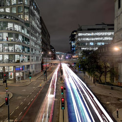 Light trails on city street amidst buildings at night