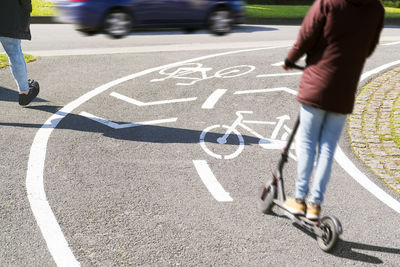 Low section of person riding push scooter on road in city