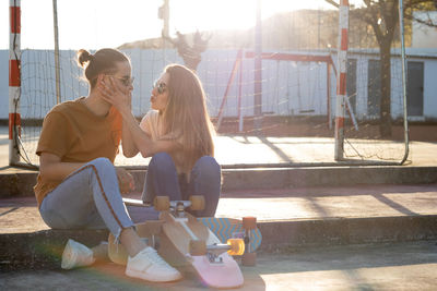 Cute young teenage couple having fun and joking with skate board around at sunset with flares around