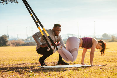 Full length of man assisting friend in exercising at public park