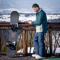 Side view of snowboarder standing on railing with a mountain view