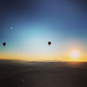 Hot air balloons flying over landscape against sky during sunset