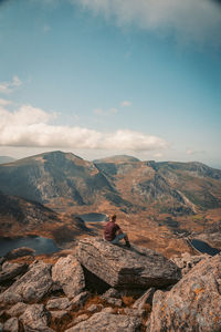 Man sitting on rock against sky