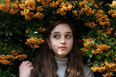 Close-up of thoughtful young woman standing against orange berries on plant