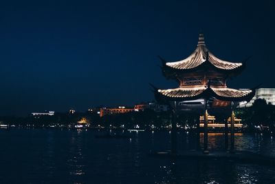 Illuminated building by lake against sky at night