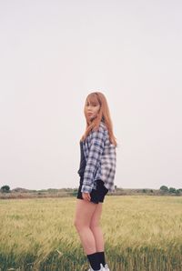 Portrait of smiling young woman standing on field against clear sky