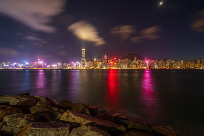 Illuminated city by sea against sky at night