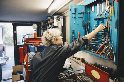 Female mechanic removing work tool from cabinet at auto repair shop