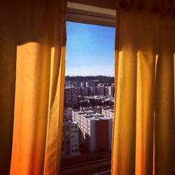 Buildings seen through window with yellow curtains