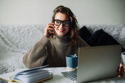 Portrait of young woman using laptop while standing against white background