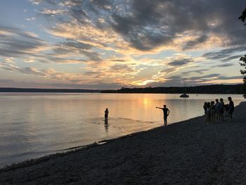 Silhouette people on beach against sky during sunset