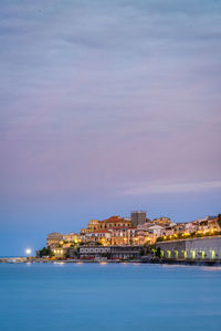 Buildings by sea against cloudy sky