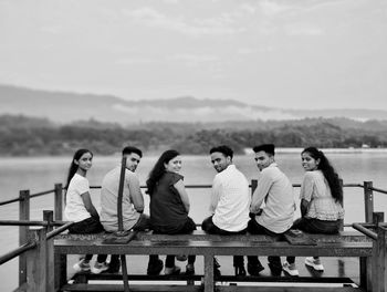 Group of friends sitting on retaining wall against sky
