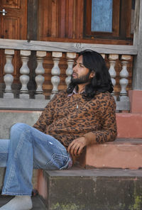  good looking indian young guy with long hair style, looking sideways while sitting on temple stairs