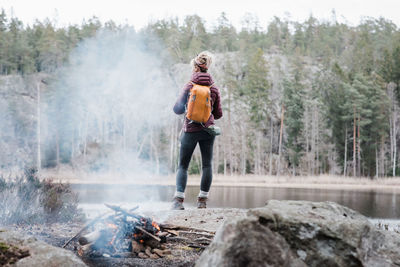 Woman standing on a rock by a campfire whilst hiking in sweden