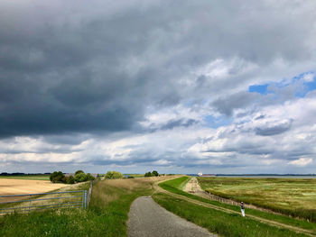 Empty road along dike against turbulent sky