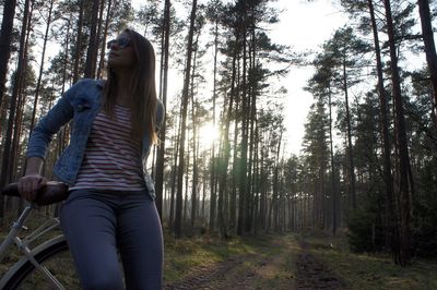 Woman sitting on bicycle against trees at forest