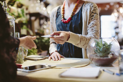 Midsection of owner taking credit card from customer for payment in plant shop