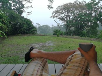 Low section of man sitting at park against sky