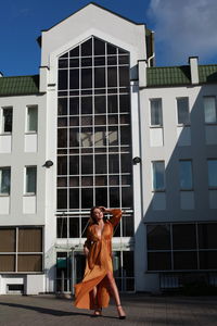 Glamorous urban photography, chic image of model in golden silk dress outdoors posing near building 