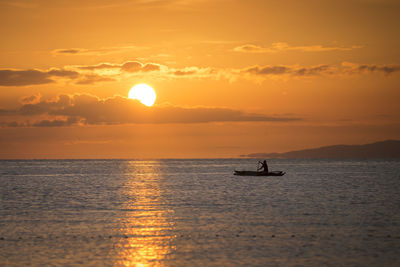 Man rowing fishing boat in sea against sky during sunset