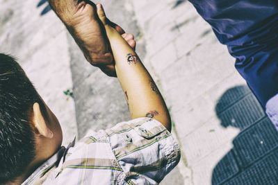 Cropped image of father holding son hand while walking on street during sunny day