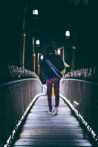 Rear view of man walking on footbridge at night