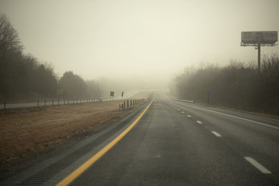 Empty road along trees against sky